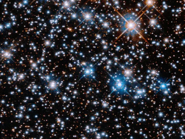 A black background is filled with small, reddish-orange stars. Larger blue-white stars are scattered across the image, with a slightly higher concentration at upper left.