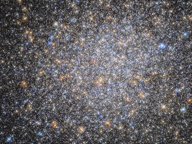The field is filled with orange, red, yellow, blue, and white stars. They appear as a spherical, dense mass that tapers out toward the edges of the image on a black background.