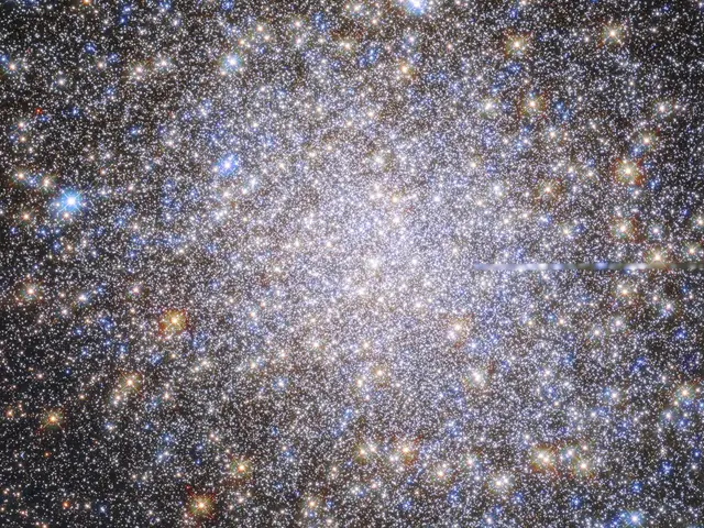 The field is filled with orange, red, yellow, blue, and white stars. They appear as a spherical, dense mass that tapers out toward the edges of the image on a black background.