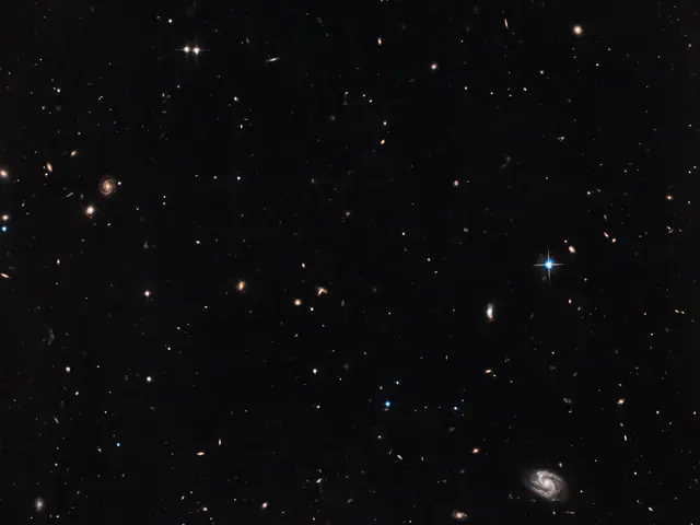 Background galaxies and stars are sprinkled across a black background. Some of the distant galaxies are spirals.