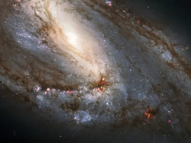 A spiral galaxy is viewed sideways, with the glowing core closer to the upper left of the image. It is surrounded by spiral arms laced through with dark dust and bright regions of star formation.