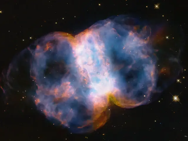 Taking up most of the image, is a multi-colored nebula in shades of blue, pink, yellow, orange, purple, and white. It appears as two translucent orbs attached by a white band.