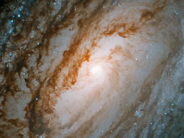 A bright galaxy core shines at the center of the image, surrounded by large spiral arms laced through with dark dust and bright blue regions of star formation.