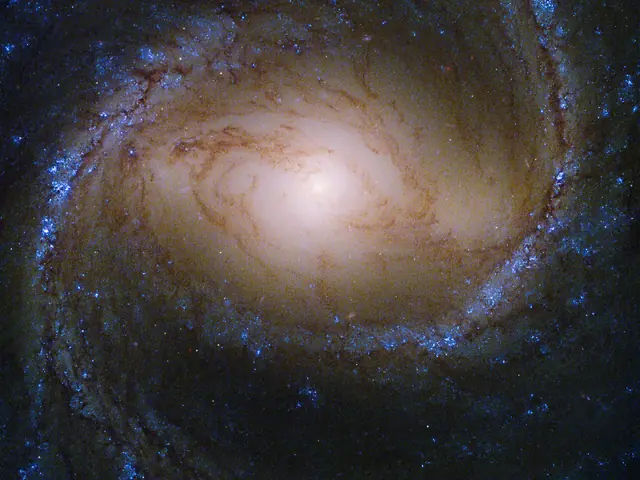 A bright yellow galaxy core shines, surrounded by spiral arms laced through with dark dust and bright blue regions of new stars.