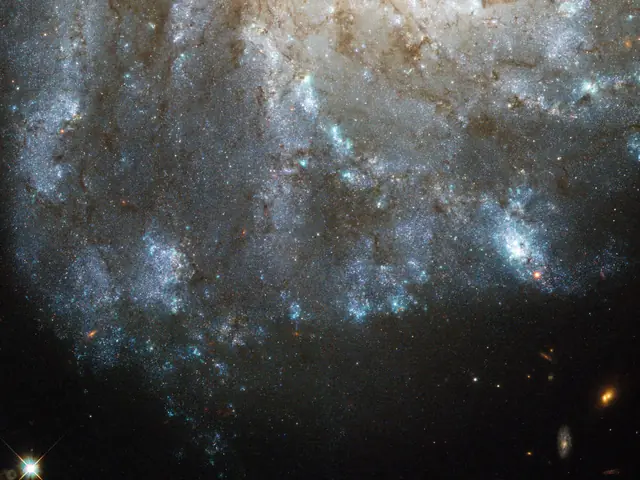 The bright blue spiraling arms of a galaxy are seen against black space, with a yellowish core visible near the top of the image.