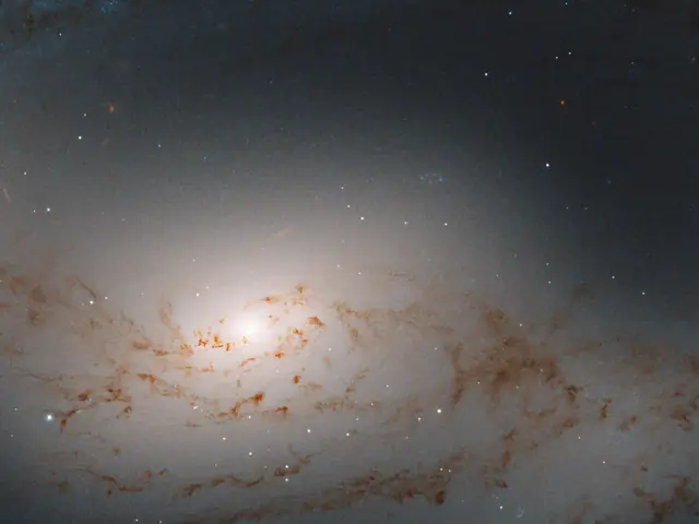Haze of light. Bright core of the galaxy just left of center. A smattering of rusty-brown dust clouds in the foreground.
